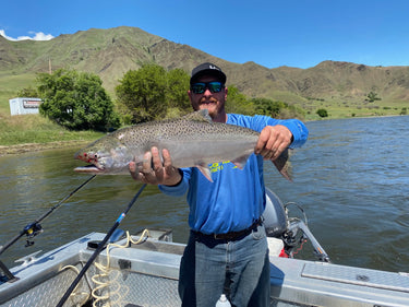 Man holding a large fish on a boat with mountains in the background